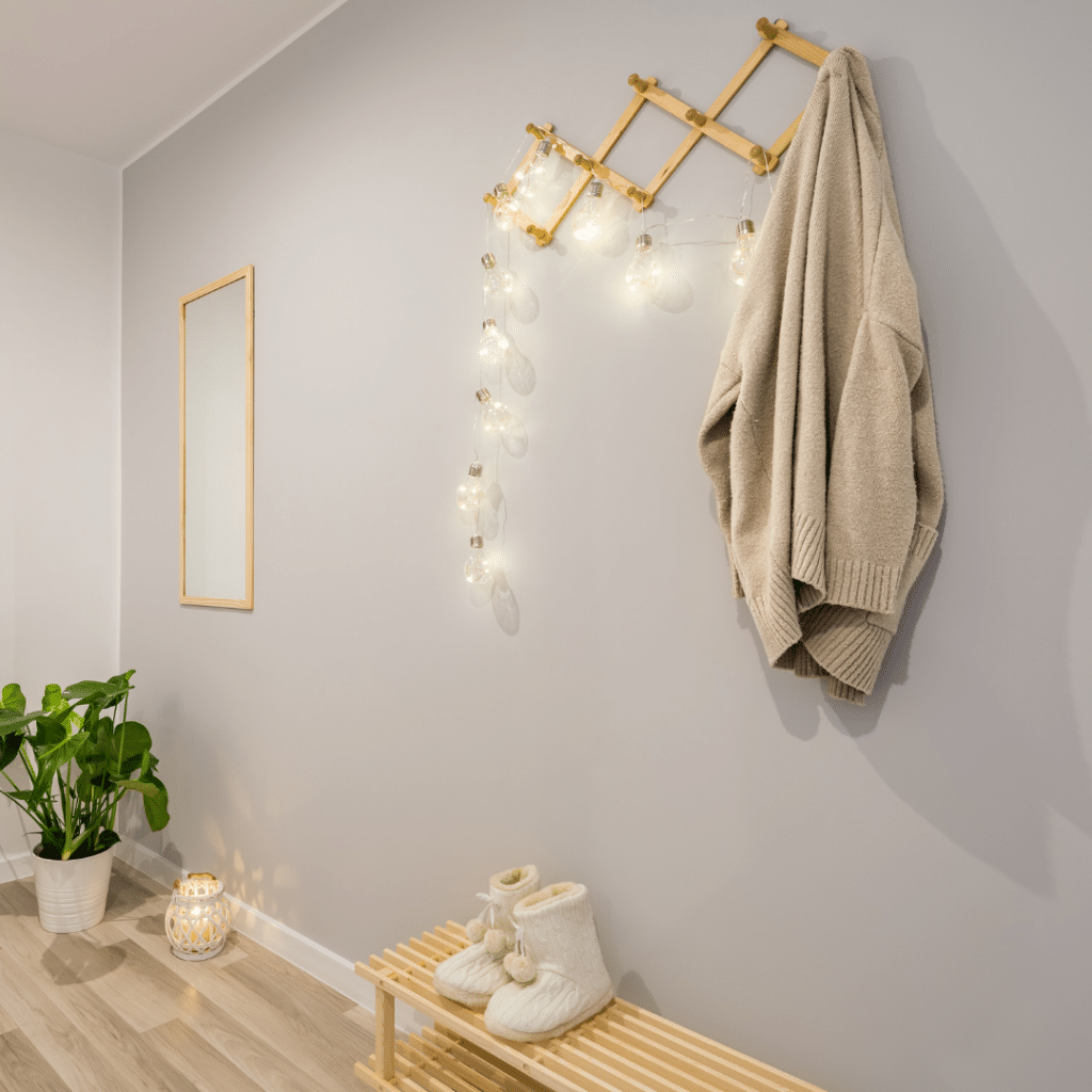 Illustrating the organizational idea that wall hooks can create storage space and personality in an entryway. Wall hooks are strung with lights in a light-colored entryway. 